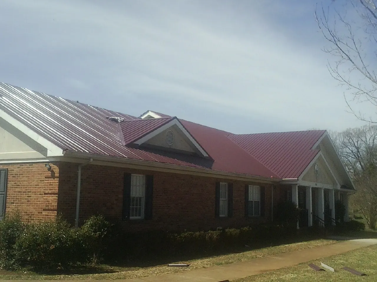 Red metal roof with gabled entries on a long brick building, from a Hail Damage Roof Repair job in Sidney