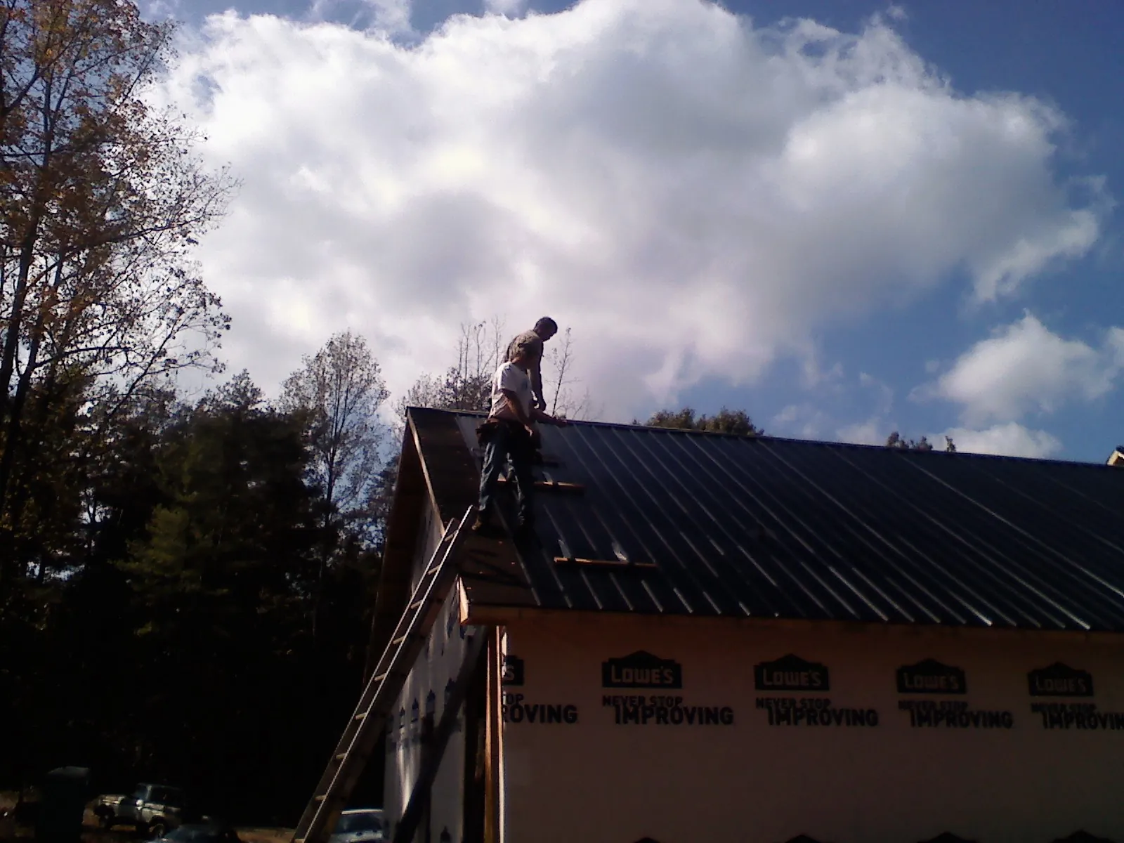 Roofer fastening dark metal panels high against a cloudy sky, from a Roof Inspection job in Sidney